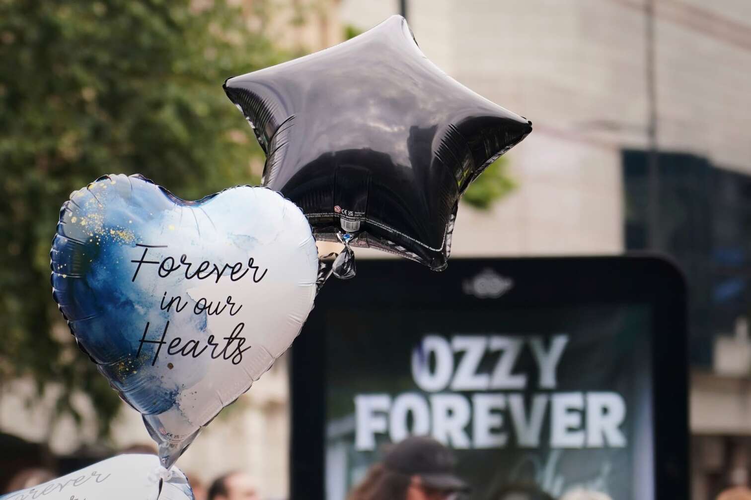 30.07.2025, Großbritannien, Birmingham: Ein Luftballon neben einem Schild zu Ehren des Musikers Ozzy Osbourne. Tausende von Fans versammeln sich, um den Trauerzug für den im Alter von 76 Jahren verstorbenen Black-Sabbath-Frontmann Ozzy Osbourne zu verfolgen. Foto: Alberto Pezzali/AP/dpa +++ dpa-Bildfunk +++