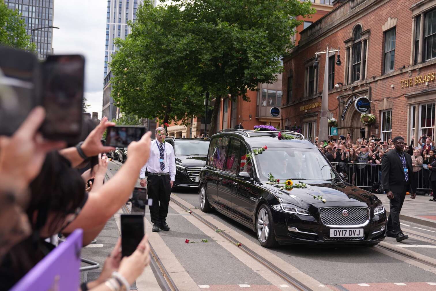 30.07.2025, Großbritannien, Birmingham: Fans beobachten den Leichenwagen mit Ozzy Osbourne auf der Broad Street. Der Leichnam des Black-Sabbath-Frontmanns wird nach seinem Tod letzte Woche im Alter von 76 Jahren zu einer Prozession in seine Heimatstadt gebracht. Foto: Joe Giddens/PA Wire/dpa +++ dpa-Bildfunk +++