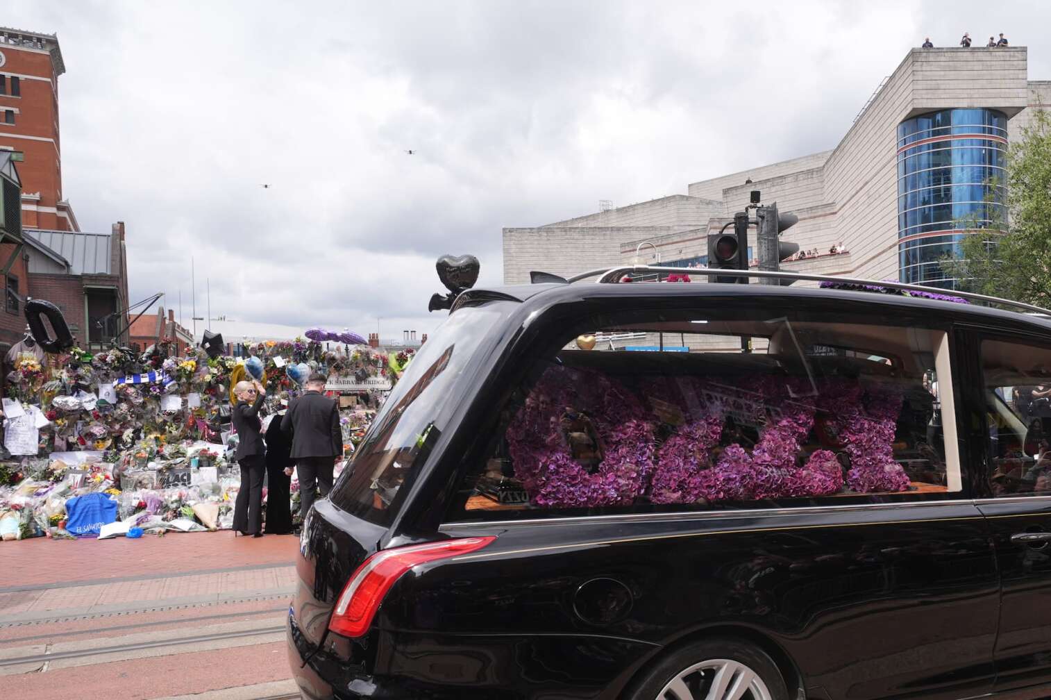 30.07.2025, Großbritannien, Birmingham: Fans beobachten den Leichenwagen mit Ozzy Osbourne auf der Broad Street. Der Leichnam des Black-Sabbath-Frontmanns wird nach seinem Tod letzte Woche im Alter von 76 Jahren zu einer Prozession in seine Heimatstadt gebracht. Foto: Joe Giddens/PA Wire/dpa +++ dpa-Bildfunk +++