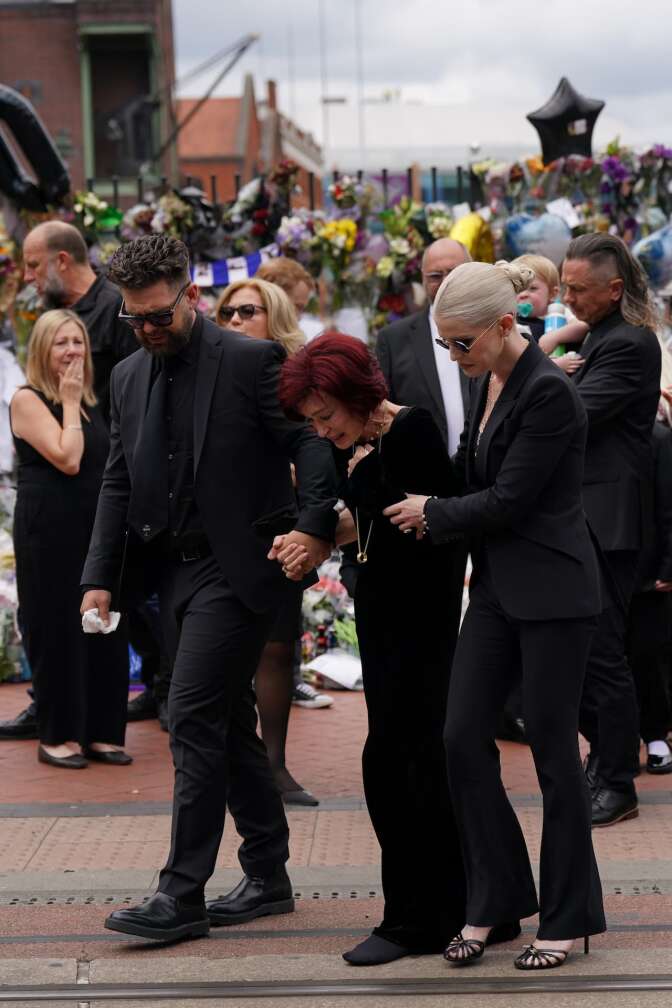 30.07.2025, Großbritannien, Birmingham: Die Familie von Ozzy Osbourne, Jack Osbourne (l-r), Sharon Osbourne und Kelly Osbourne legen Blumen nieder und betrachten die Botschaften und Blumenspenden, die an der Black-Sabbath-Brücke in der Broad Street zum Gedenken an den Black-Sabbath-Frontmann Ozzy Osbourne hinterlassen wurden, während sein Leichnam nach seinem Tod letzte Woche im Alter von 76 Jahren für eine Prozession in seine Heimatstadt zurückgebracht wird. Foto: Joe Giddens/PA Wire/dpa +++ dpa-Bildfunk +++