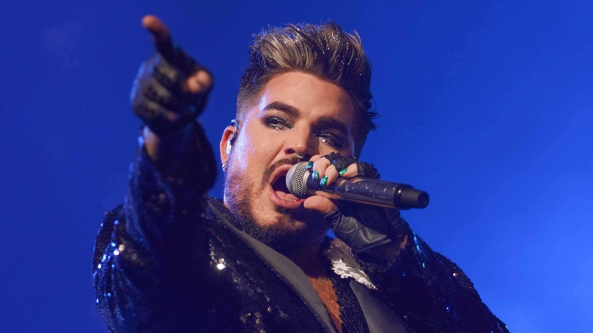 Adam Lambert mit glitzernden Haaren und Mikrofon auf der Bühne